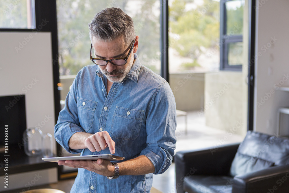 Caucasian man standing in livingroom using digital tablet Caucasian man standing in livingroom using digital tablet