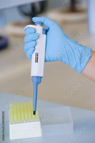 Scientist working in chemical laboratory with automatic pipette. Wearing blue gloves.