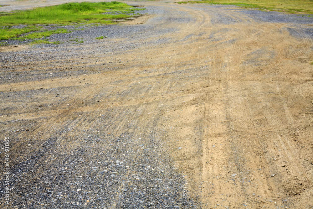 car wheel trail on the ground and gravel floor with grass field