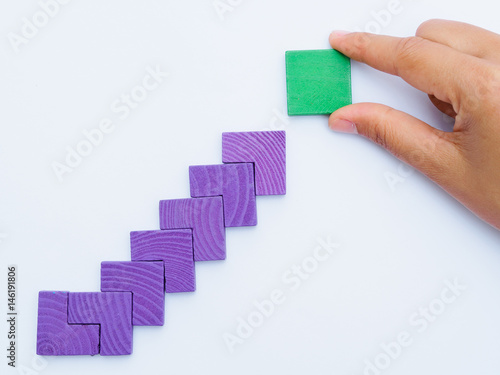 Concept of building success foundation. Women hand put difference color of puzzle wooden blocks in the shape of a staircase