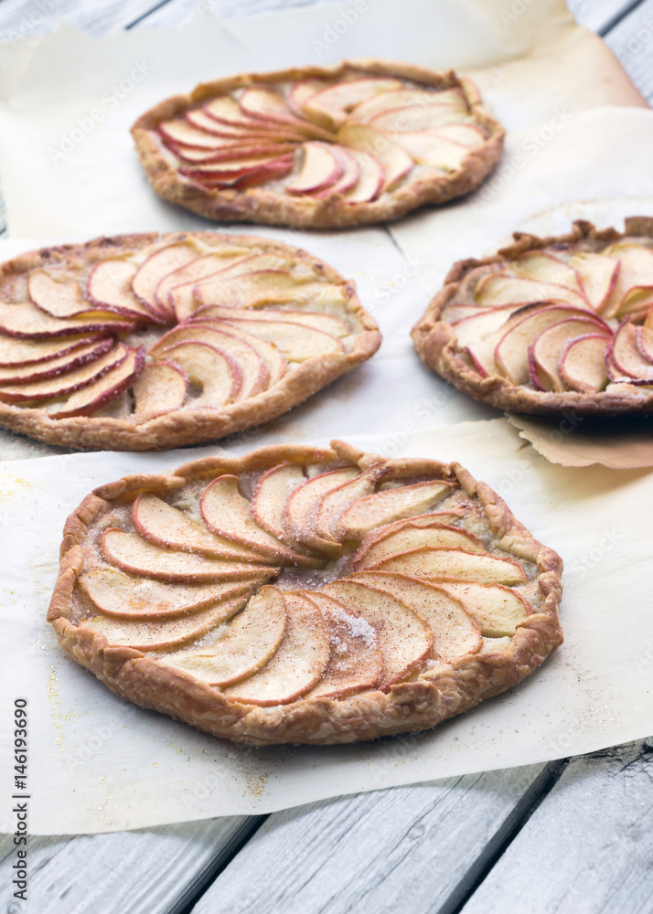 Apple pie on the thin crust with sugar and cinnamon. Apple tart with ricotta cheese and cinnamon. Round pies on the white wooden background. Apple's slices. Piece of pie. Apple pie on the thin crust with sugar and cinnamon. Apple tart with ricotta cheese and cinnamon. Round pies on the white wooden background. Apple's slices. Piece of pie.