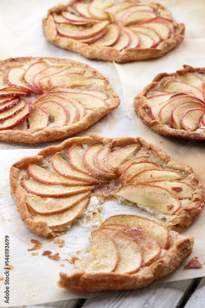 Apple pie on the thin crust with sugar and cinnamon. Apple tart with ricotta cheese and cinnamon. Round pies on the white wooden background. Apple's slices. Piece of pie.
