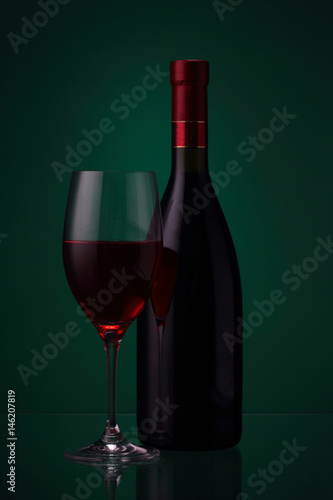Bottle of red wine and glass on green