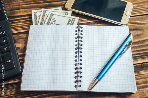 on wooden background is the phone Notepad pen calculator and dollars photo