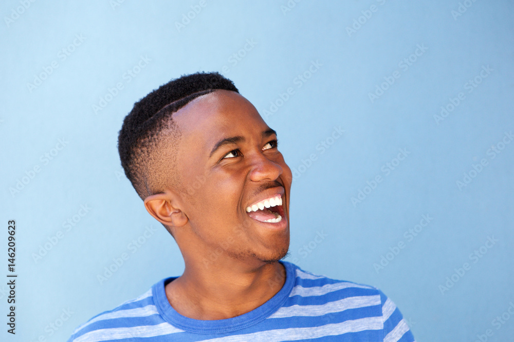 Close up young african man laughing against blue wall Close up young african man laughing against blue wall