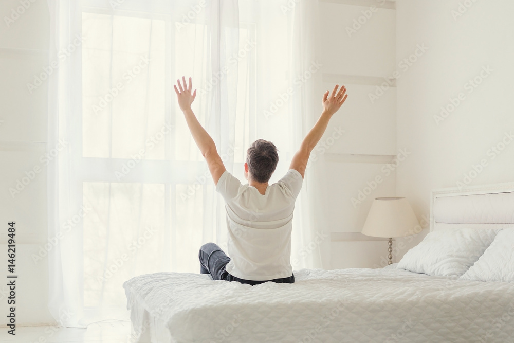 Man sitting on bed in bedroom with hands raised up in the morning. Ready for a brand new day