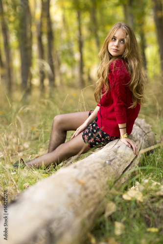 Portrait of a young blonde female on field sitting on a tree trunk.