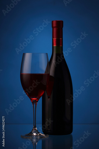 Wineglass and bottle with red wine on blue