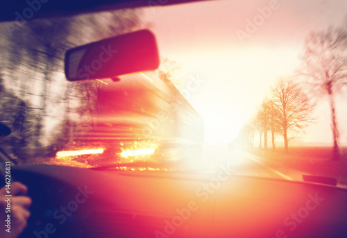 Driving a car in the morning against sunrise, passing a truck