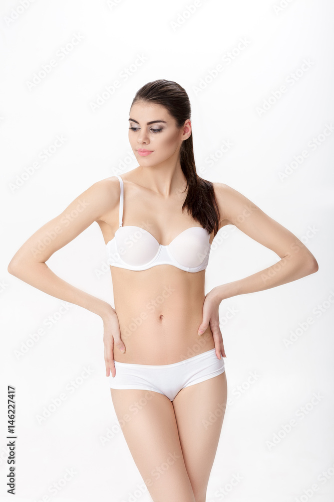 Fototapeta premium beautiful young brunette woman with perfect sporty body in white lingerie on white background
