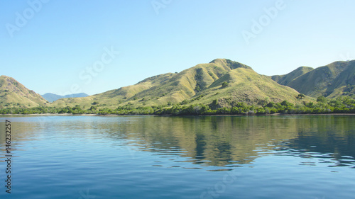 Coastline of mountains with green vegetation reflected in blue ocean water at Labuan Bajo in Flores, Indonesia.