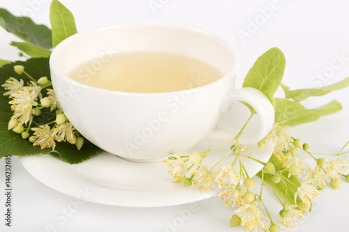 Hot linden tea in a fine white porcelain cup, studio shot over white background. Large-leaved Linden, Tilia platyphyllos.