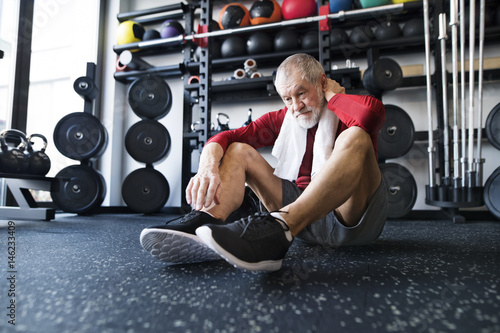 Exhausted senior man sitting on the floor after working out in gym photo