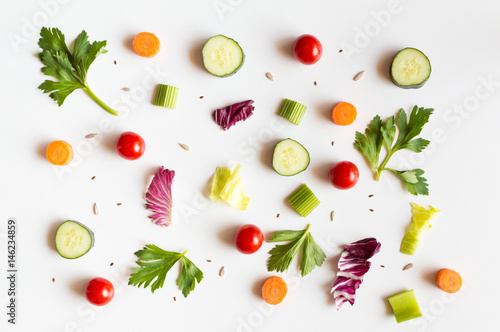 Eating pattern with raw ingredients of salad, lettuce leaves, cucumbers, red tomatoes, carrots, celery and seeds on white background