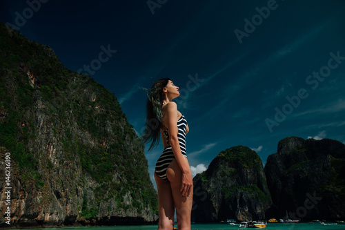 Fashion portrait of a beautiful sexy girl in a striped swimsuit in a paradise bay. photo