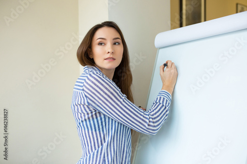 Serious girl standing with a marker near a whiteboard and drawing. Business, startup, planning, manager woman start writing on a flipchart