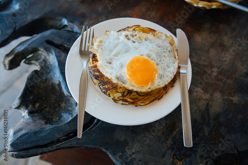 Potato pancakes with fried eggs are served with a knife and fork. On the oak table. Cafe by the sea. photo