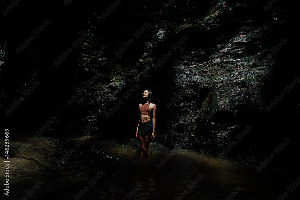 beautiful wet girl in shorts and a knitted blouse against a waterfall background. Dark background. beautiful wet girl in shorts and a knitted blouse against a waterfall background. Dark background.