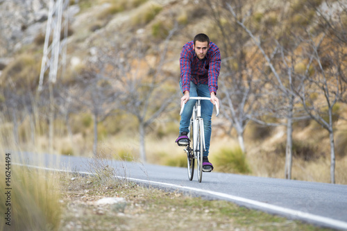 Cyclist man riding fixed gear sport bike in sunny day on a mountain road