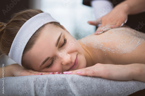 Young smiling woman getting firming sugar scrub therapy on her back