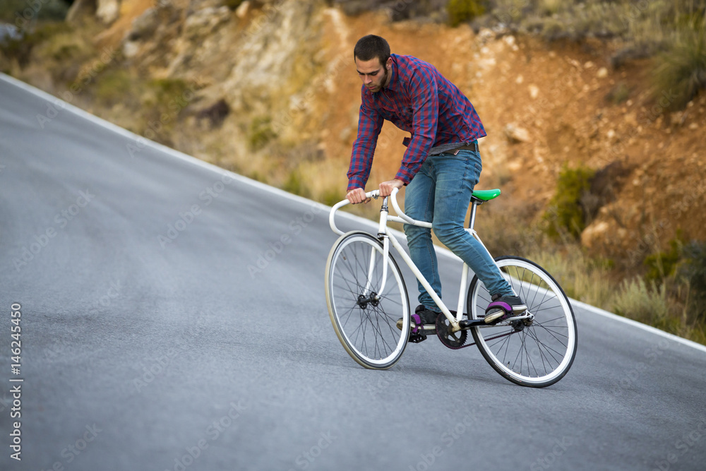 Cyclist man riding fixed gear sport bike in sunny day on a mountain road