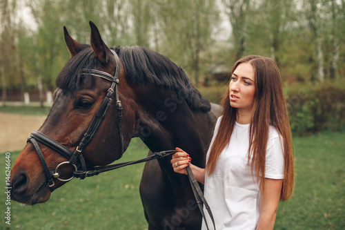 Beautiful girl communicates with the horse in the park. Preparing for the riding