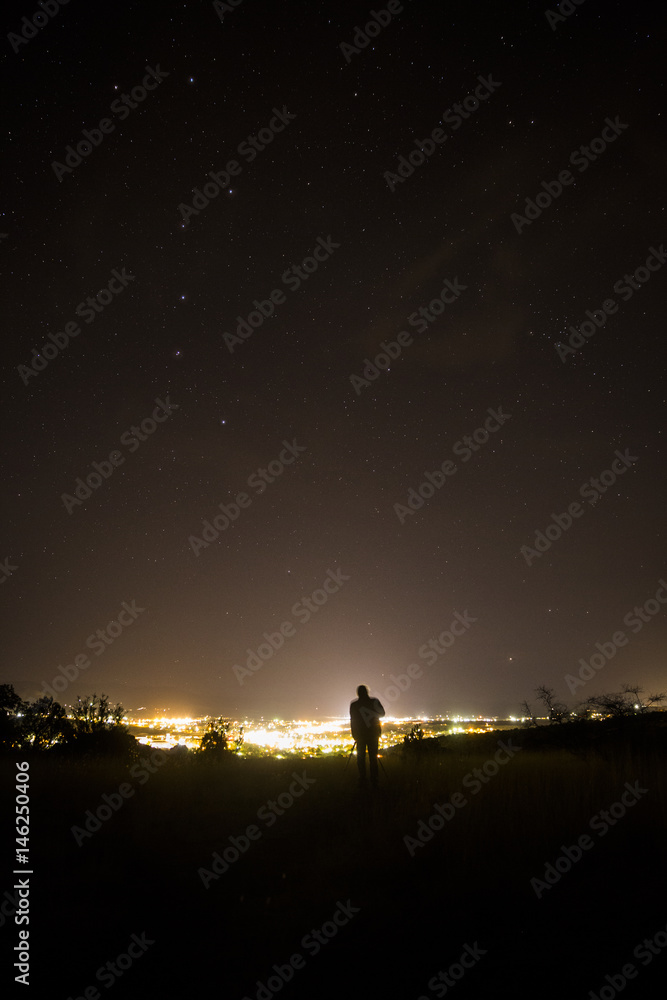 photographer shooting the stars over a small mountain town 