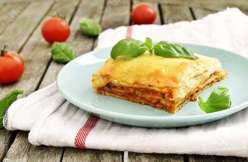 Fresh meat lasagne, lasagne bolognese, pasta dish on a wooden table with decorative basil leaf. Italian cuisine.