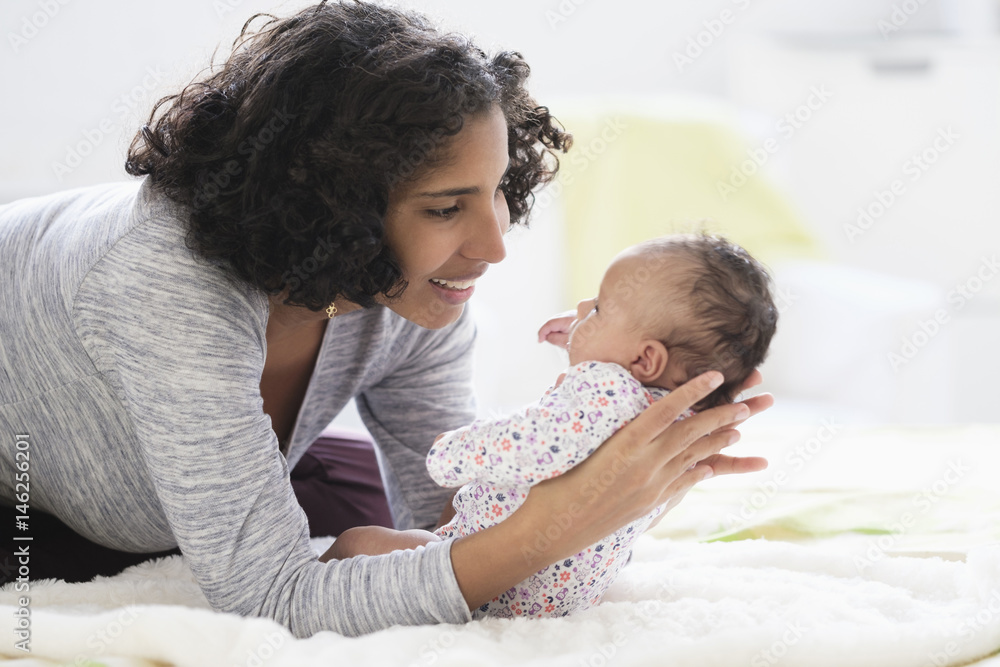 Hispanic mother laying on bed holding baby daughter Hispanic mother laying on bed holding baby daughter