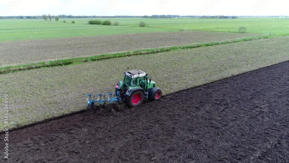 Aerial near modern tractor ploughing also known as plowing land a plough or plow is tool farm implement used in farming for cultivation of soil in preparation for sowing seed planting to loosen soil Aerial near modern tractor ploughing also known as plowing land a plough or plow is tool farm implement used in farming for cultivation of soil in preparation for sowing seed planting to loosen soil