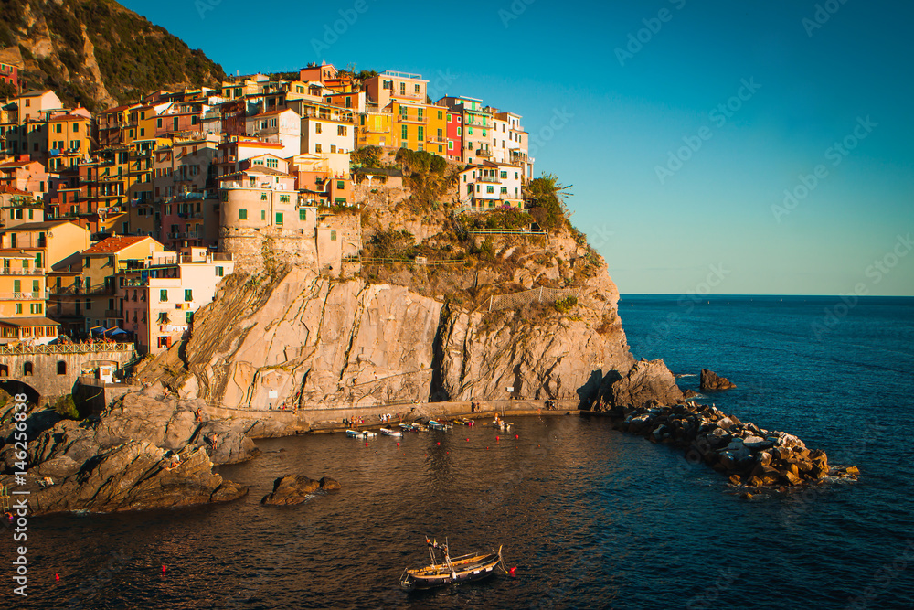 Village of Manarola, Cinque terre, at sunset landscape. A small boat in the sea. Soft orange-yellow sunset light on the landscape.