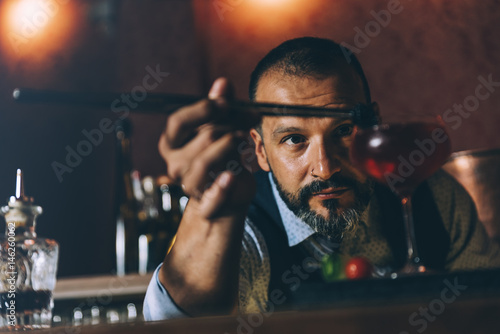 Barman is making cocktail at night club.