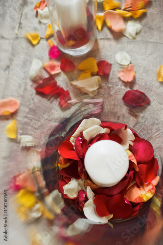 Look from above at white candle standing on red and yellow rose petals