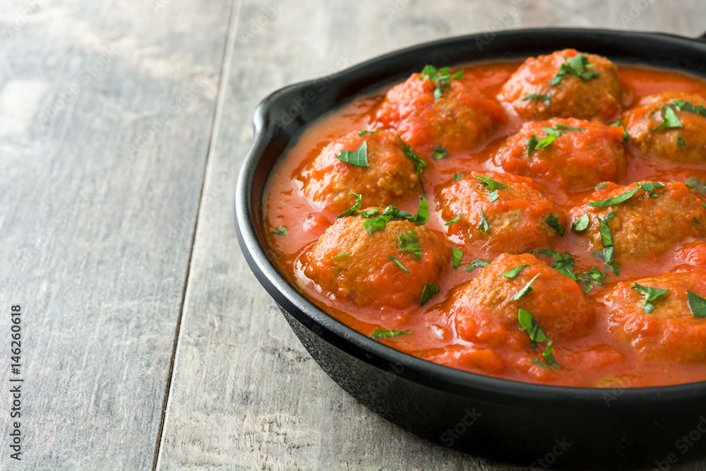 Meatballs with tomato sauce in iron frying pan on wooden table