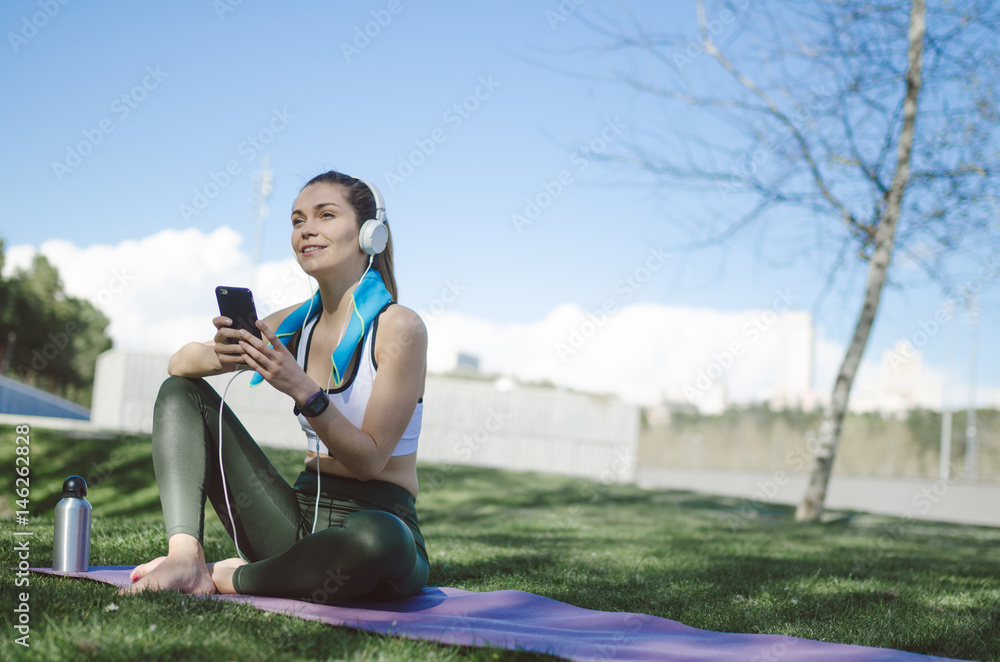healthy woman resting and listening music with mobile phone while doing yoga and workout