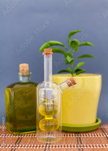 Two glass bottles olive oil stands near a flower against a dark background