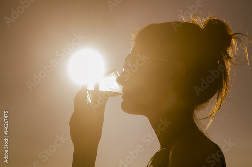 Young attractive woman on the beach at sunset drinking from glass photo