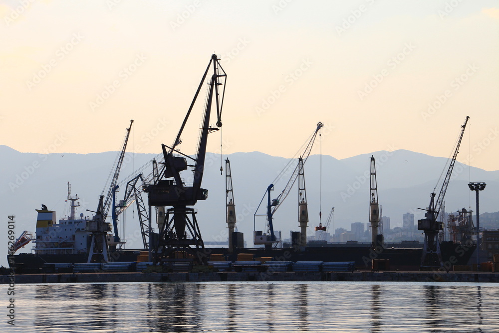 Silhouette of port cranes and a bulk carrier ship in the harbor with Ucka mountain, Istria, in the background at sunset, city of Rijeka, Croatia, Europe