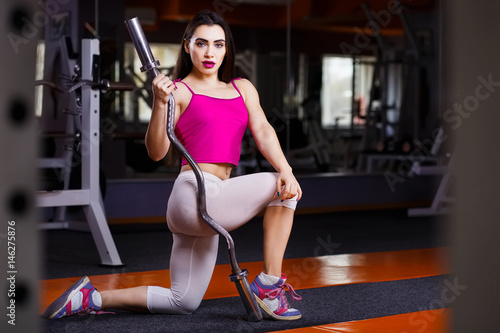 Young attractive muscular sexy fitness woman posing with barbell in gym