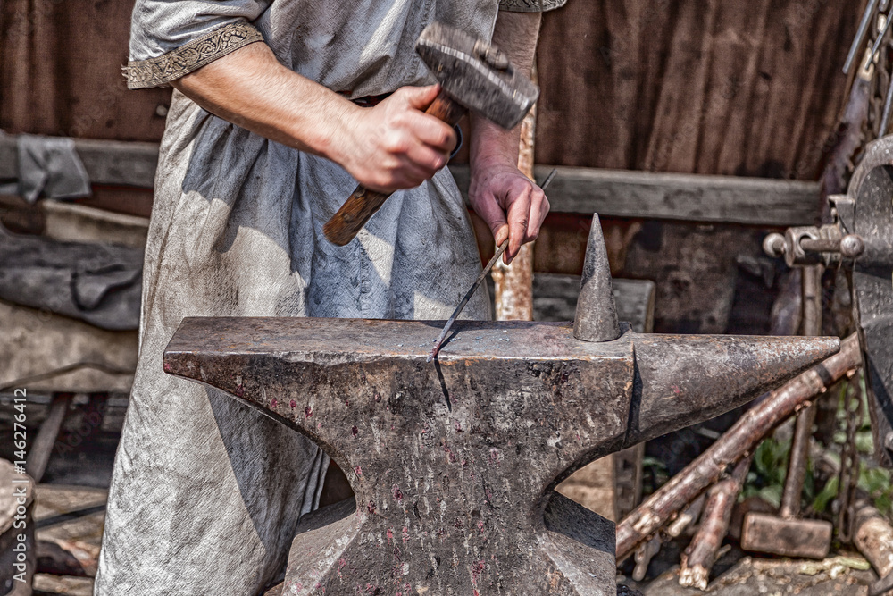 Medieval blacksmith at work with hammer and anvil.