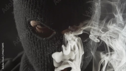 dangerous terrorist in a balaclava smokes e-cigarette vape and makes a lot of smoke. photo
