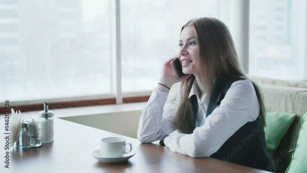 One business woman is sitting in a cafe and smiling and talking on the phone One business woman is sitting in a cafe and smiling and talking on the phone