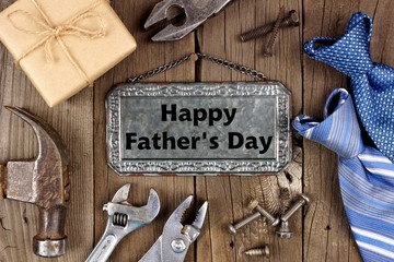 Happy Fathers Day message on metal sign with frame of tools, gifts and ties on a wooden background
