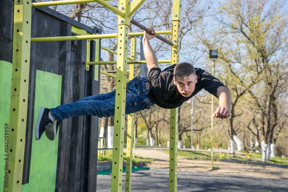 Fit man cross training on monkey bars . Fitness workout on brachiation  ladder in an outdoor gym outside. Male athlete hanging on one hand doing  back lever one arm Stock Photo