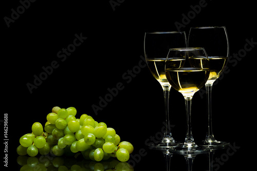 Glasses for wine and a bunch of grapes on a black background
