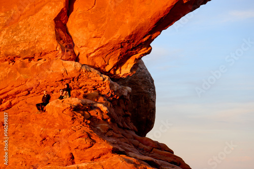 People sitting at Turret Arch through the North Window at sunrise in Arches National Park near Moab, Utah
