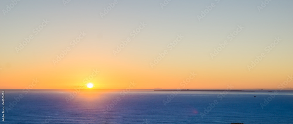 Abstract effect defocused background image Orange glow of sunrise sitting on horizon over blue sea panorama.
