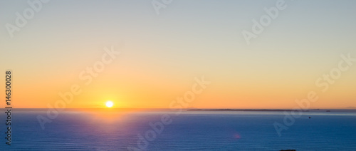 Abstract effect defocused background image Orange glow of sunrise sitting on horizon over blue sea panorama. © Brian Scantlebury