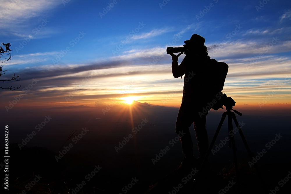 Silhouette of the photographer on a hillside on a background of clouds