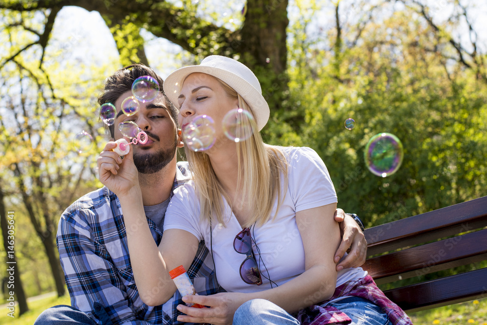 Couple having fun in the park while blowing soup bubbles on beautiful sunny day